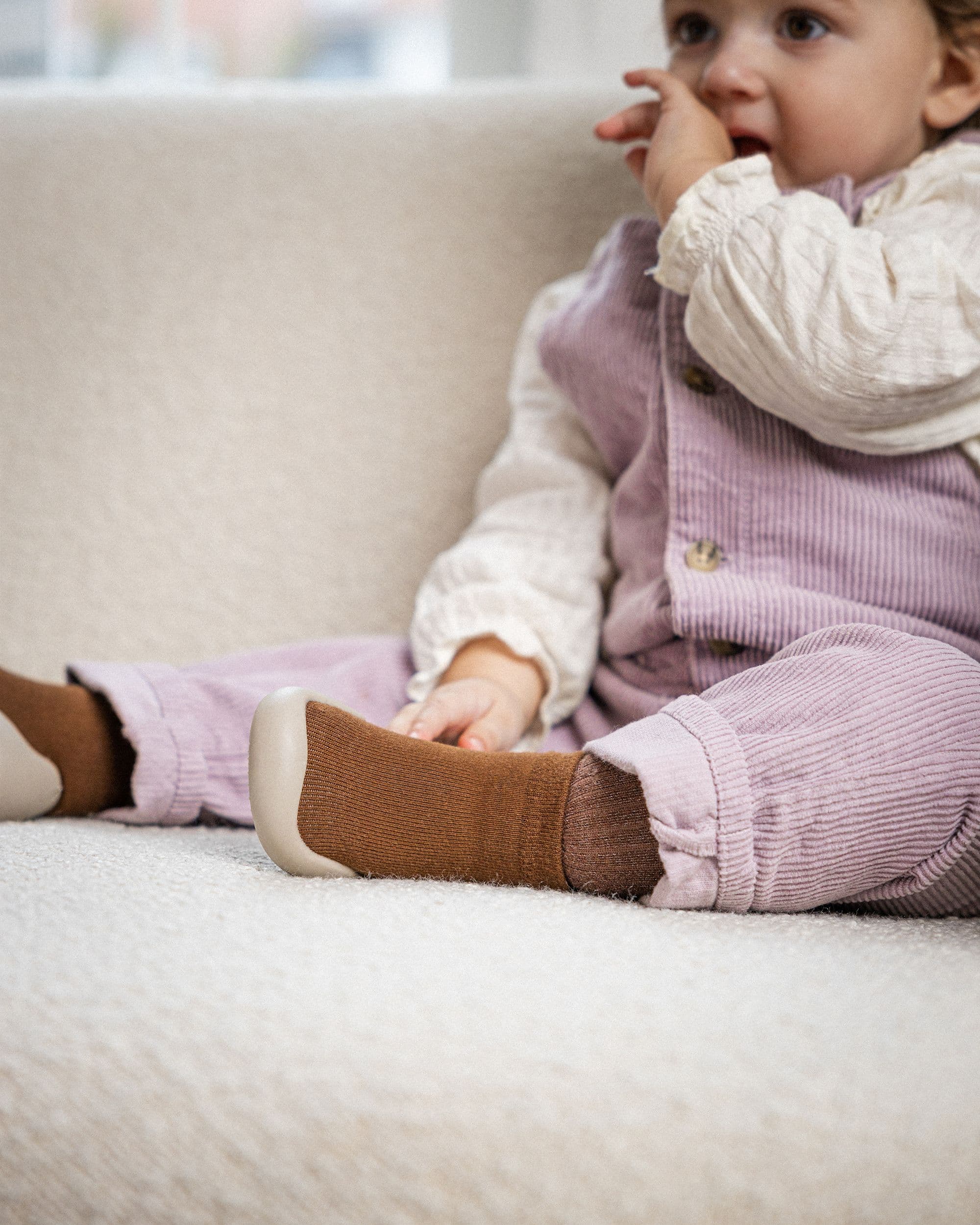 Baby iført brun strømpesko med skridsikker sål, perfekt til indendørs leg og komfort.