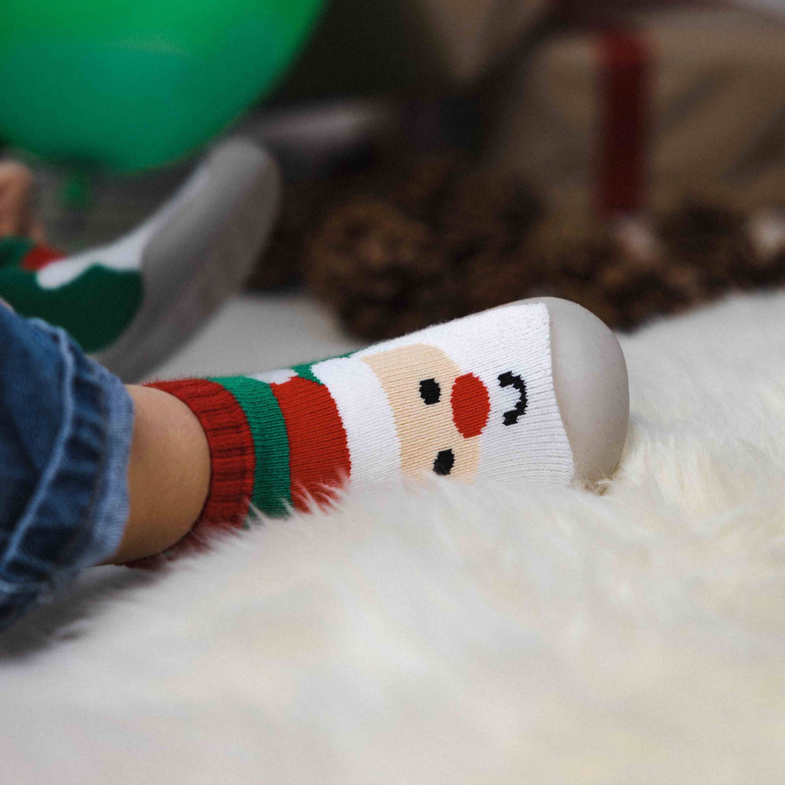 Begyndersko med julemandsmotiv og skridsikker sål, båret af barn på blødt tæppe.