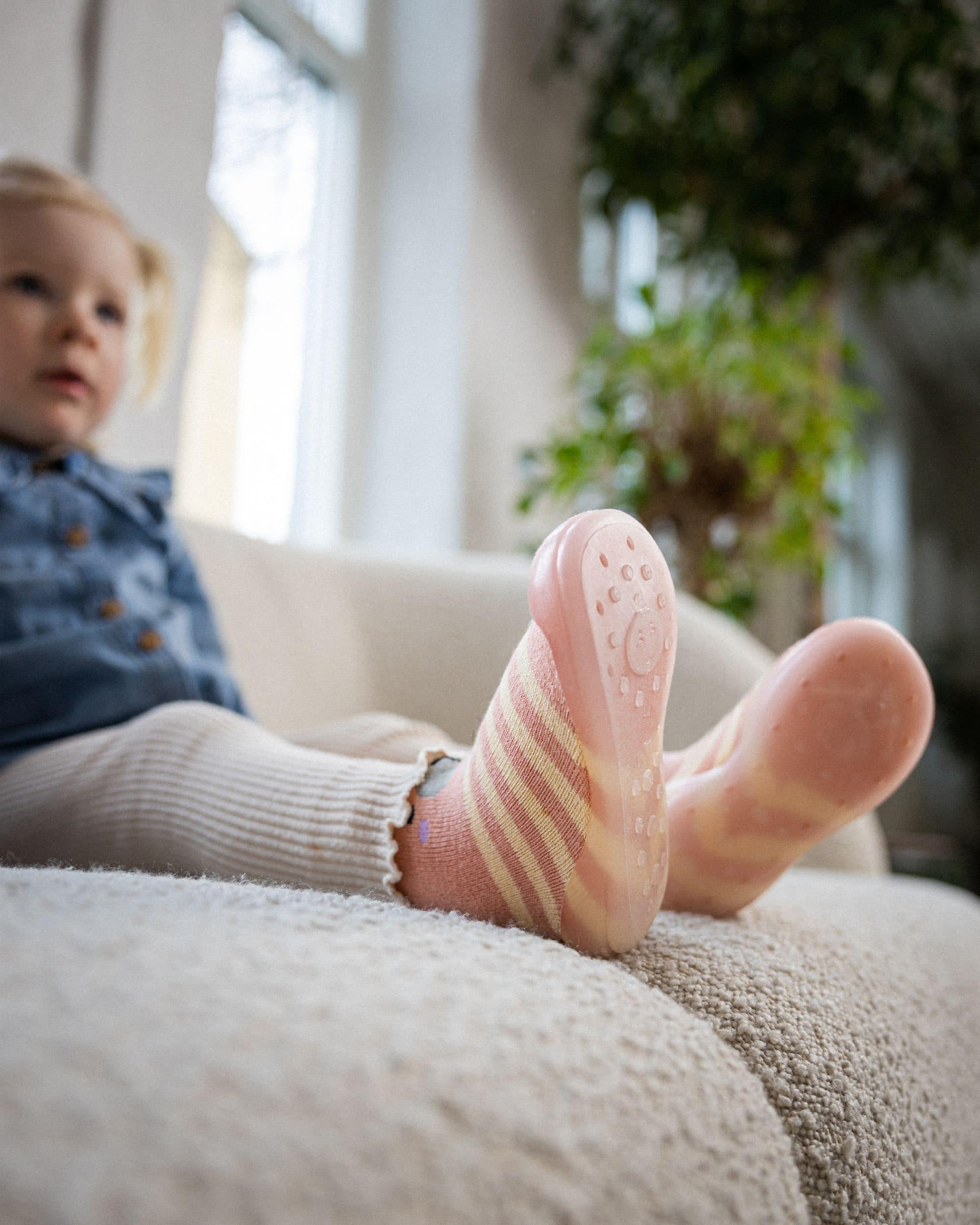 Lyserøde begyndersko med skridsikker sål på barn i sofa – perfekte til små fødder i bevægelse